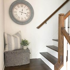 a clock mounted on the wall above some stairs with a basket and plant in it