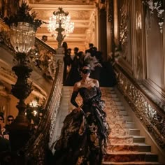 a woman in a black and gold dress is walking down the stairs