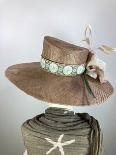 This Dark tan/mocha brown women's straw hat is so pretty! It is completely handmade, hand blocked and one of a kind. The hat is embellished with a lovely French ribbon with a blue, brown, tan and ivory circular floral motif. It is perfect for summer through fall. Her name is Emmaline. The Wide brim makes a statement, as does the slightly asymmetrical crown. Embellished with an oversize vintage flower and fluttery soft tan feathers. A great ladies hat that stands apart from mass produced ones. Dr Fitted Brown Boater Hat For Spring, High Crown Straw Hat For Vacation, Elegant Handmade Flat Brim Straw Hat, Chic Brown Boater Hat For Kentucky Derby, Elegant Brown Boater Hat For Summer, Elegant Handwoven Wide Brim Boater Hat, Elegant Handmade Panama Hat With Curved Brim, Brown Curved Brim Top Hat For Kentucky Derby, Artisan Wide Brim Brown Top Hat