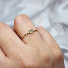 a person's hand with a heart shaped ring on their left finger, wearing a gold band