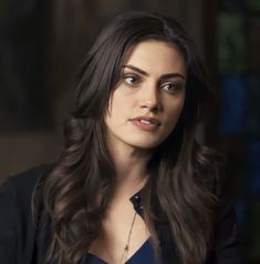 a woman with long dark hair wearing a black shirt and necklace looking at the camera