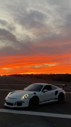 a white sports car parked in an empty parking lot with the sun setting behind it