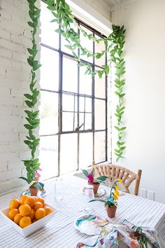 the table is set with oranges and place settings in front of an open window