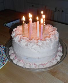 a birthday cake with pink frosting and five lit candles on it, sitting on a table