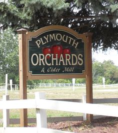 the sign for plymouth orchards and cider mill is in front of a white fence