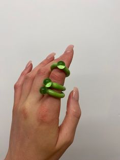 a woman's hand is holding two green rings in the shape of three fingers