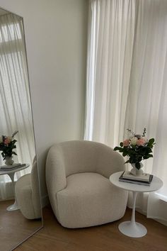 a white chair sitting in front of a mirror next to a table with flowers on it