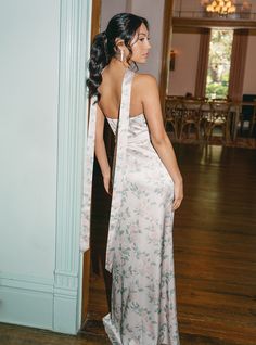 a woman in a long dress standing on a wooden floor next to a wall and doorway