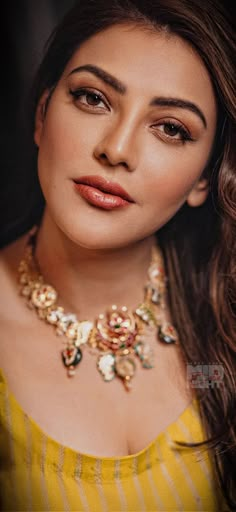 a woman wearing a yellow top with a necklace on her neck and gold jewelry around her neck