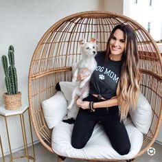 a woman sitting in a chair holding a small white dog and smiling at the camera