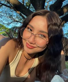 a woman wearing glasses sitting under a tree with her hair blowing in the wind and smiling at the camera