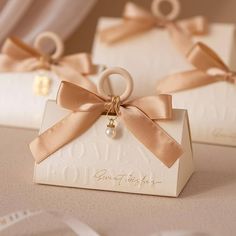 two small white boxes with gold ribbons and pearls on them are sitting on a table