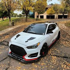 a white car parked on the side of a road in front of trees and leaves