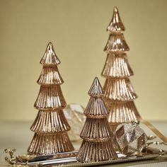 three small christmas trees sitting on top of a table next to a silver tray with a gold ribbon