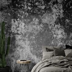 a bed sitting next to a green cactus on top of a wooden table in front of a gray wall