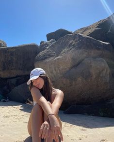 a woman sitting on top of a sandy beach next to large rocks in the background