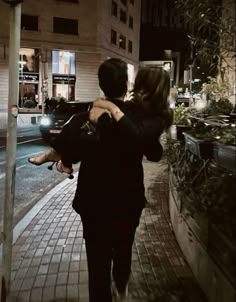 a man carrying a woman on his back walking down the street at night with buildings in the background