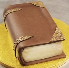 a cake made to look like a book on top of a yellow plate with gold trim