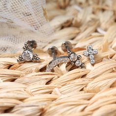 two pairs of diamond earrings sitting on top of a woven basket next to each other