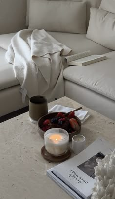 a white couch sitting next to a table with a bowl of fruit on top of it