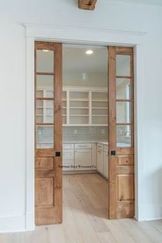 an open door leading to a kitchen with white cabinets and wood floors in a house