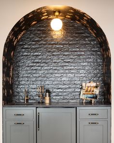 a kitchen area with gray cabinets and an arched brick wall above the countertop is lit by a light fixture