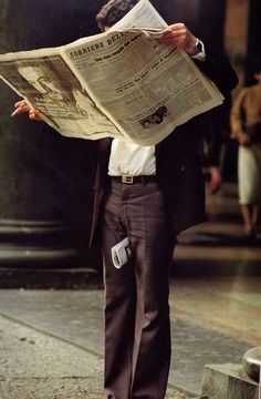 a man standing on the sidewalk reading a newspaper