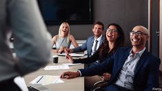 a group of people sitting around a conference table smiling at someone on the computer screen