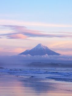 a snow covered mountain is in the distance as clouds hover over the ocean and beach