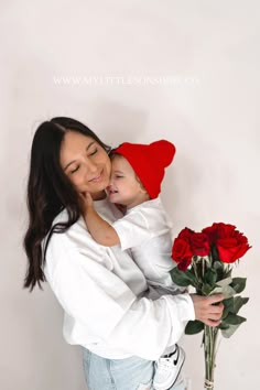 a woman holding a baby in her arms next to a vase with roses on it