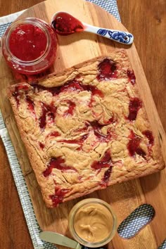 a wooden cutting board topped with strawberry cobbler next to two jars of peanut butter