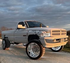 a silver truck parked on the side of a road next to grass and trees with clouds in the background