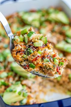 a spoon full of food that is being lifted from a casserole dish with cucumbers and other vegetables