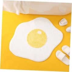 a fried egg on a yellow surface next to white slippers and an orange towel