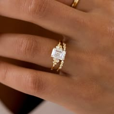 a woman's hand with two gold rings on it and an engagement ring in the middle