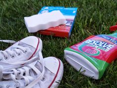 two pairs of shoes are laying on the grass next to toilet paper and toothpaste