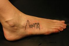 a small tattoo on the foot of a person with a city skyline in the background