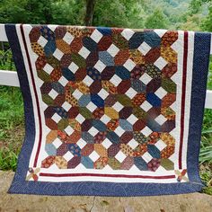 a quilt hanging on a fence in front of some trees