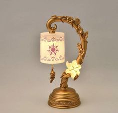 a gold lamp with a white shade on it's base and a flower decoration