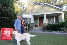 a man and woman standing in front of a house with a dog next to a for sale sign