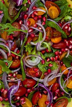 a salad with tomatoes, onions and spinach on a yellow plate next to some other vegetables