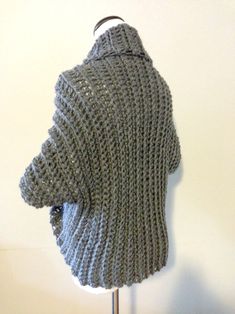 a gray knitted sweater hanging on a white coat hanger next to a wall