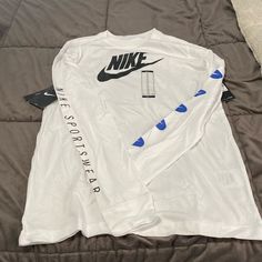 Nwt White Long Sleeve Nike Tee. The Left Sleeve Is Adorned With 5 Blue And White Nike Swoosh Emblems And The Right Arm Has Nike Sportswear Written Down It. The Back Of The Shirt Has The Nike Emblem Written Backwards. Nike Tee, Nike Tees, Nike Swoosh, White Nike, Boys Top, Nike White, Kids Nike, Nike Shirts, White Nikes