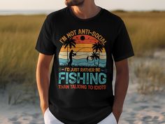 "Embrace your passion for solitude and fishing with this humor-filled graphic tee. Featuring the silhouette of a serene fisherman against a vibrant sunset backdrop and the words \"I'm Not Anti-Social, I'd Just Rather Be Fishing Than Talking To Idiots\", this shirt is perfect for those who find peace by the water. Made from comfortable materials, it's ideal for casual outings, beach trips, or a day out on the boat. A great gift for anglers, introverts, or anyone who enjoys a good laugh. Ready to wear, it's sure to be a conversation starter and a favorite wardrobe staple for any fishing enthusiast." Summer Fishing T-shirt With Crew Neck, Summer Crew Neck T-shirt For Fishing, Crew Neck T-shirt For Summer Fishing, Fisherman Silhouette, Outdoor Wardrobe, Sunset Backdrop, Angel T Shirt, Casual Beach Wear, Fisherman Gifts