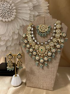 a necklace and earring set on display next to a white flower vase with flowers in the background