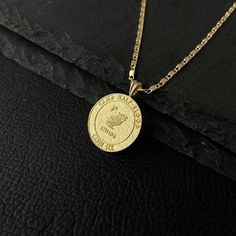 a gold necklace with a medallion on the front and back, sitting on a black leather surface