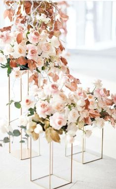 three gold vases filled with flowers on top of a white tablecloth covered floor