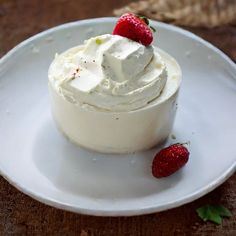 a white plate topped with a cake covered in whipped cream and two strawberries next to it