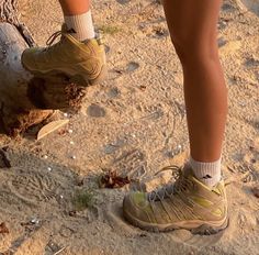 a person standing on top of a sandy beach next to a tree trunk and wearing hiking shoes