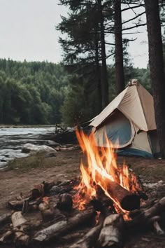 a tent is set up next to a campfire in the woods near a river